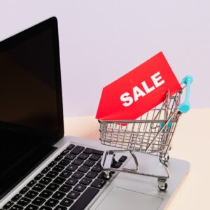 Laptop with tiny shopping cart holding a red "SALE" tag suggesting a Cyber Monday sale