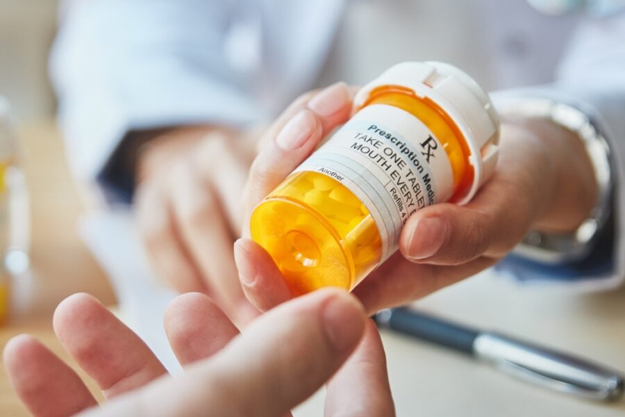 Photo of pharmacist's hands passing prescription bottle to someone.