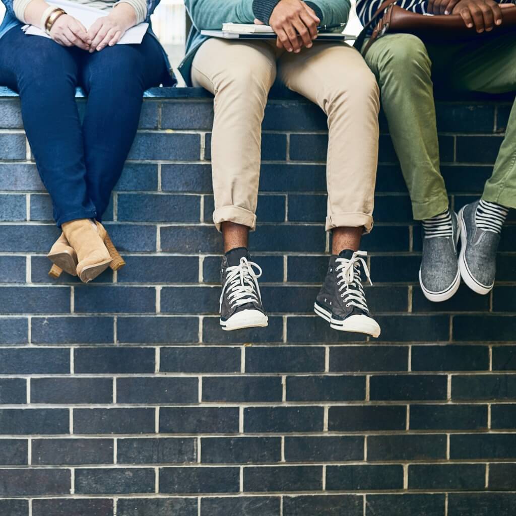 Photo of a brick wall showing legs of students wearing the best shoes for college.