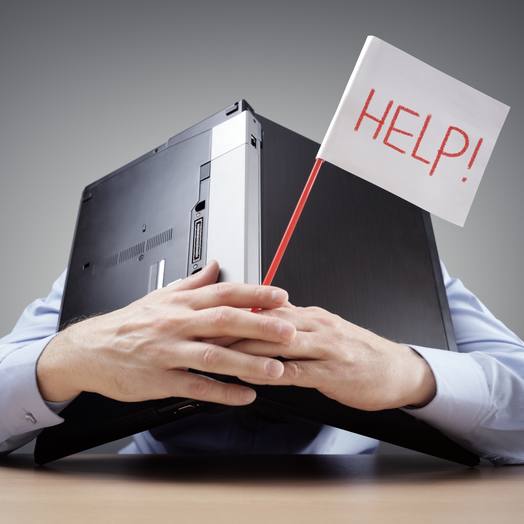 Work stressed man with laptop holding up a sign that reads "HELP!"