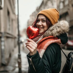 Young woman in winter coat holding a small red heart-shaped balloon.