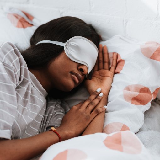Dark-skinned woman in bed asleep wearing a sleep mask.
