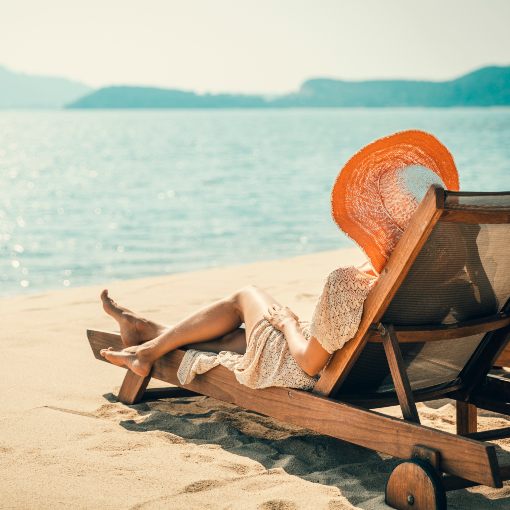 Woman in a sun hat relaxing on the beach in a lounge chair.