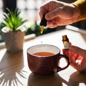 Man's hands shown adding CBD oil to tea with a dropper.