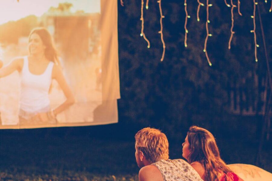 Young couple lying in their backyard on a blanket in summer watching a movie on an outdoor screen.
