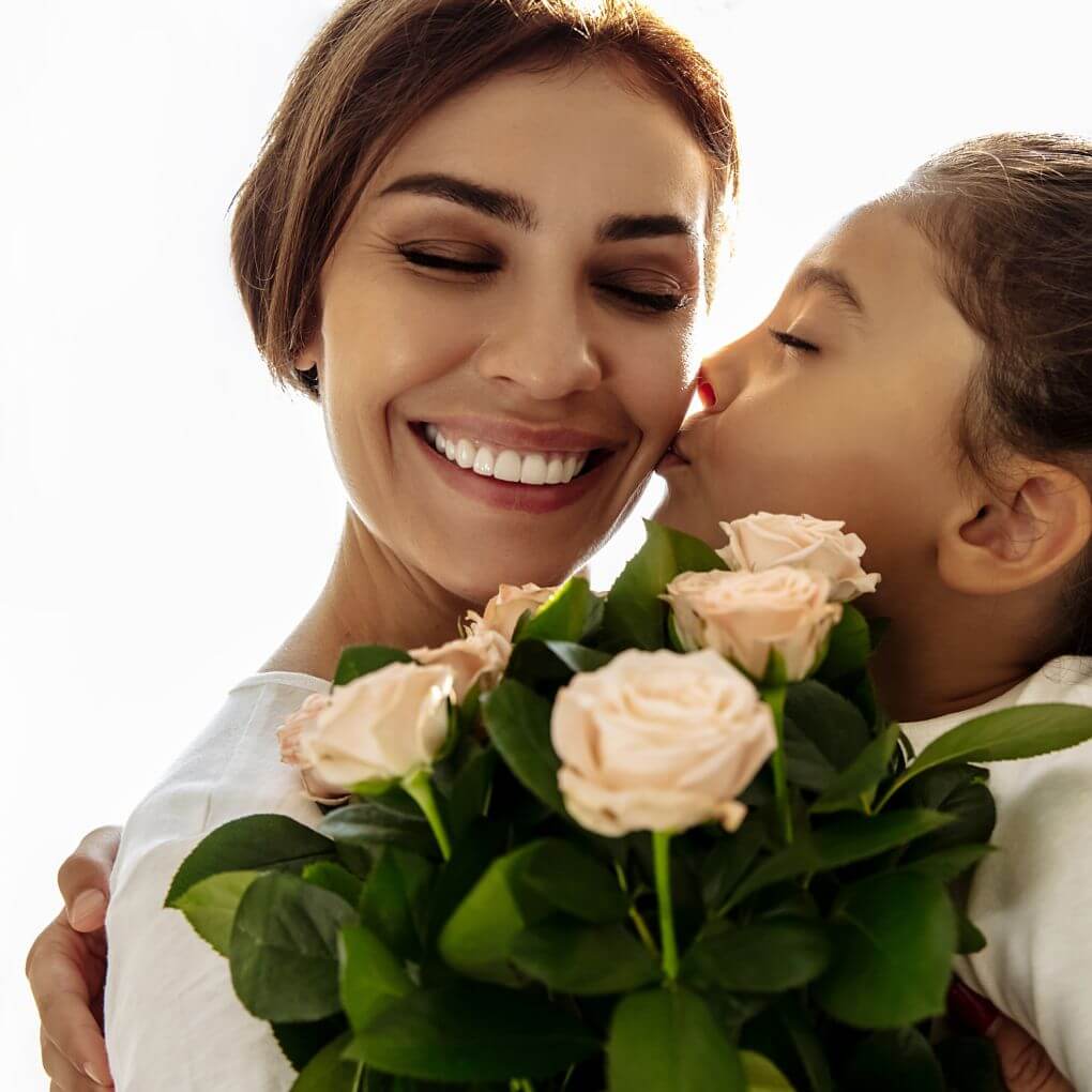 A child hugging her mom and giving her a bouquet of pink roses