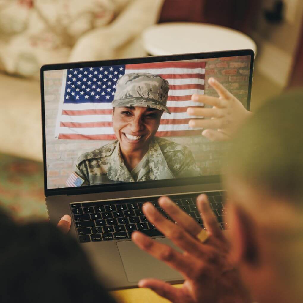 Military mom in fatigues chatting with her family on a video call.