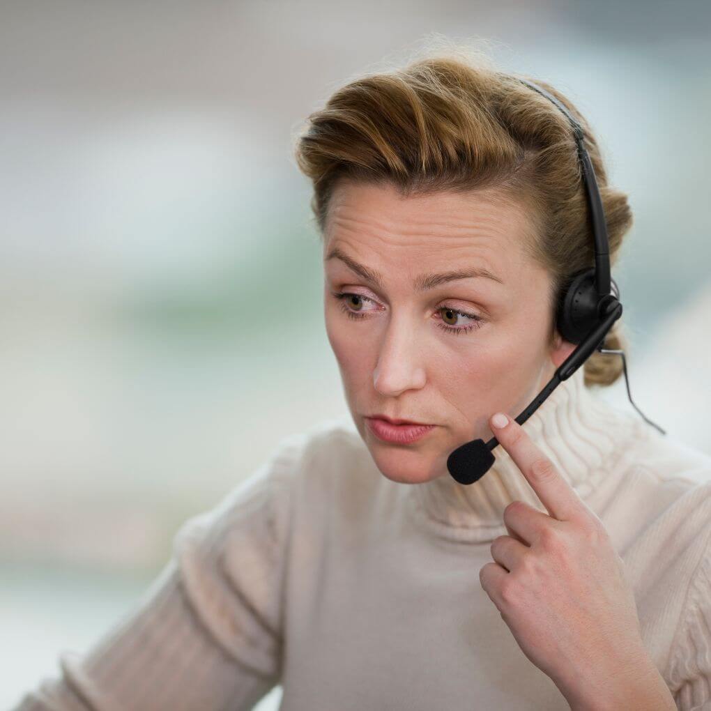 Image of a female 911 dispatcher with a headset taking a call and looking concerned.
