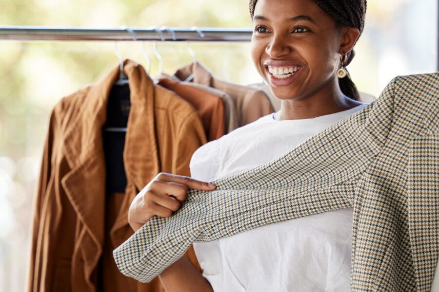 Young Black woman in a dressing room smiling and trying on a checked blazer.