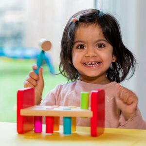 Cute toddler girl playing with a wooden peg toy and smiling.