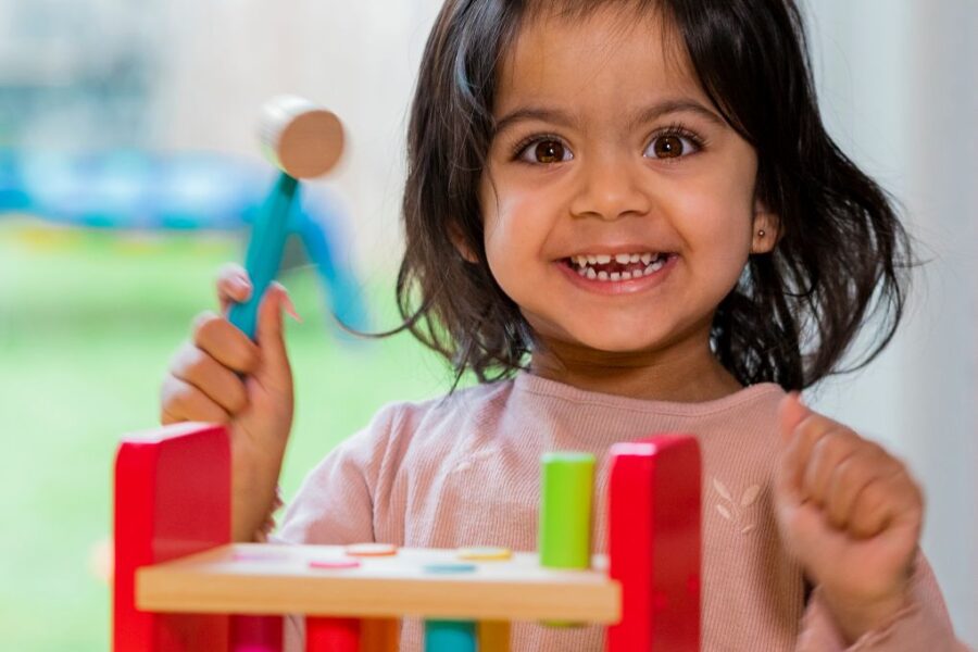 Cute toddler girl playing with a wooden peg toy and smiling.