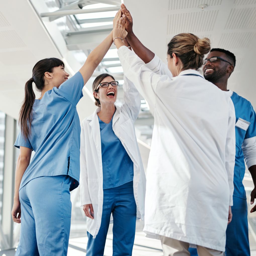 Group of nurses and doctors giving each other a high five in a hospital hallway.