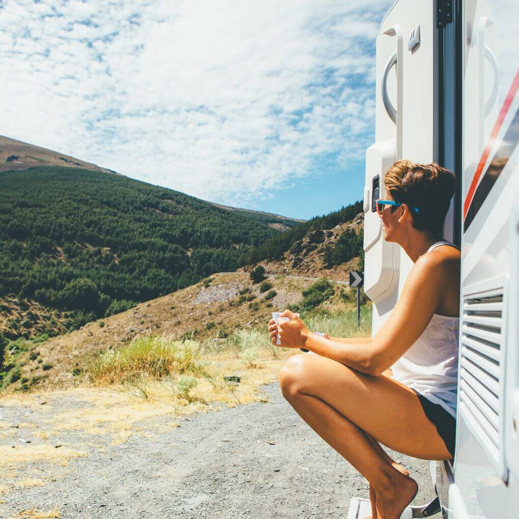 Woman sitting on the doorstep of a rental RV overlooking a national park.
