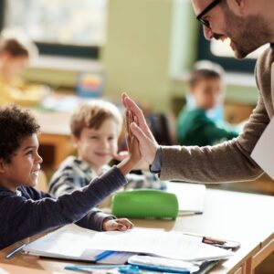 Happy male teacher giving high-five to his black elementary student in the classroom.