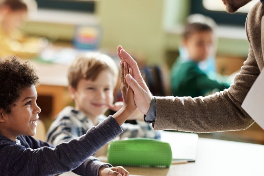 Happy male teacher giving high-five to his black elementary student in the classroom.