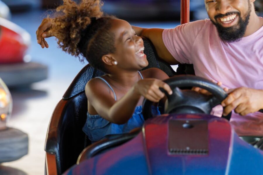A Beautiful Little Daughter is Happy to Spend a Wonderful Day with her Happy Father. They are Driving an Electric Car in the Amusement Park.
