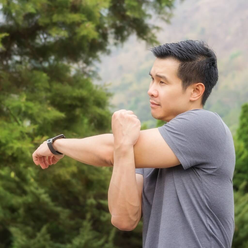 Asian man in a gray t-shirt doing stretches outdoors.