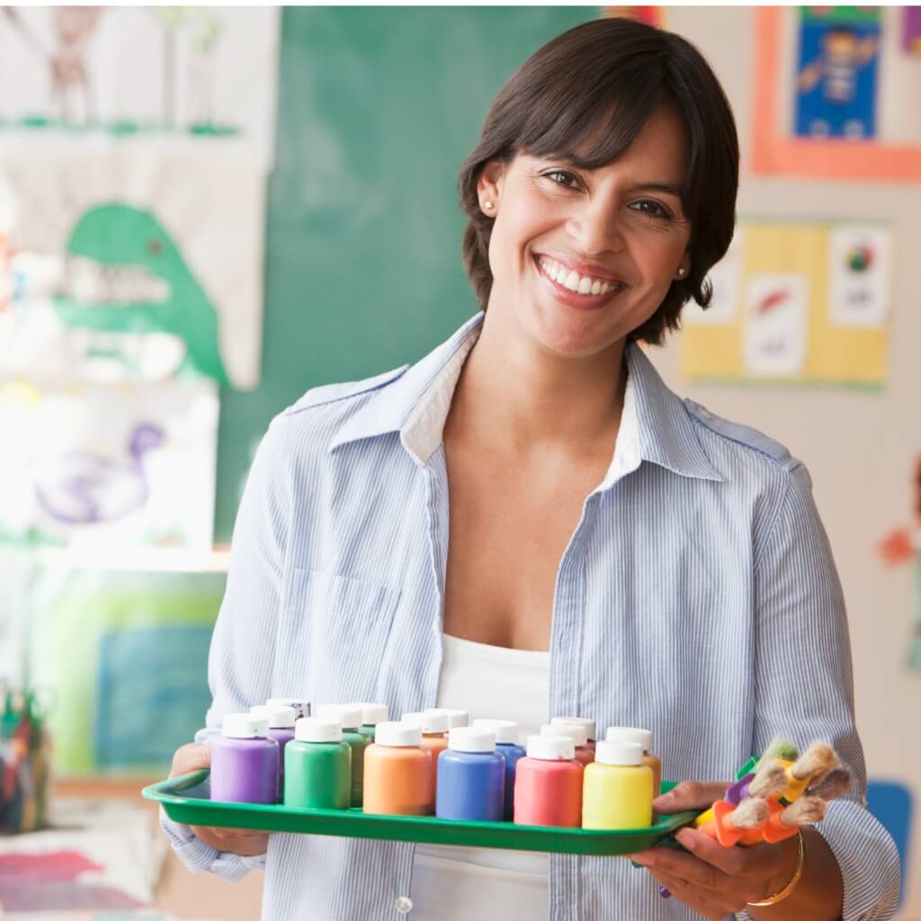 Teacher in classroom doing classroom setup with a tray full of tempera paints.