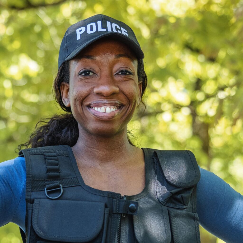 A smiling black female police officer in a blue hat that says "POLICE"