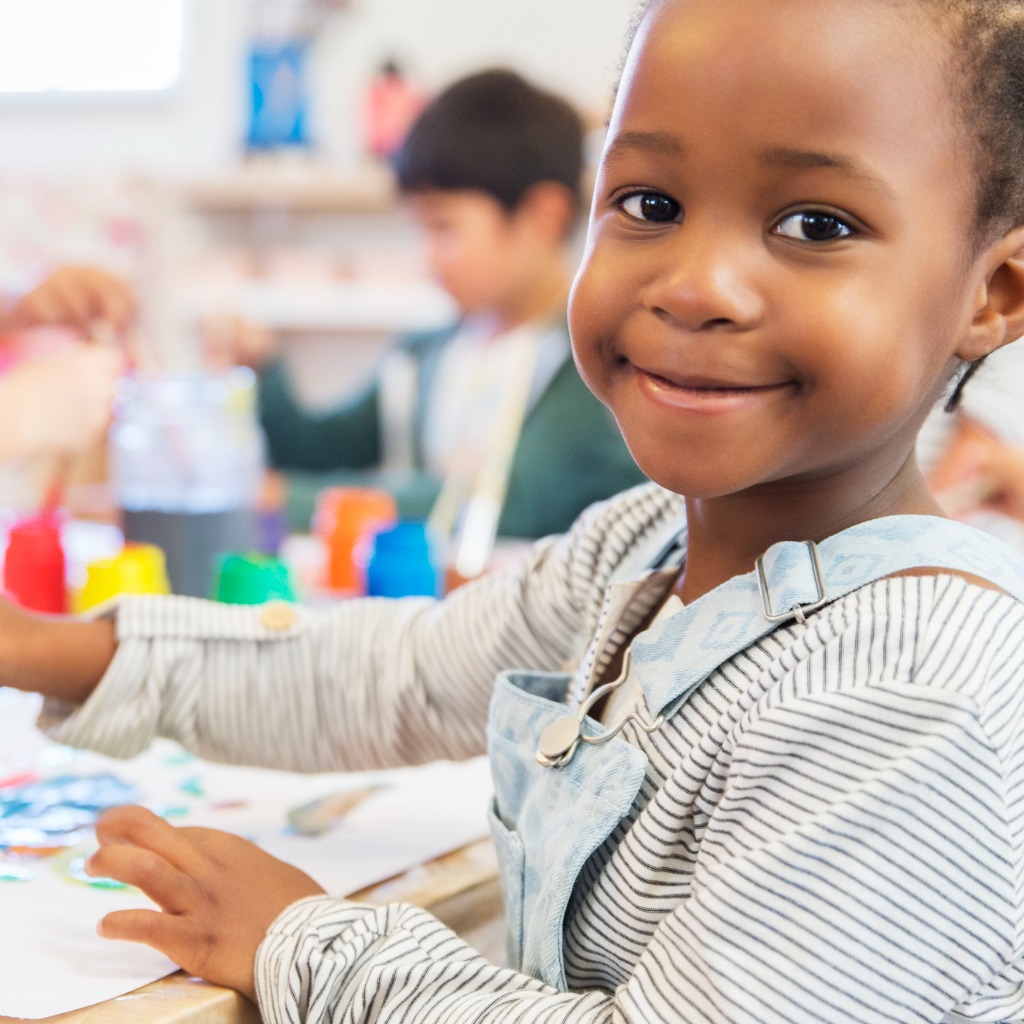 Smiling Black child in a Purple Star school classroom setting making a painting.