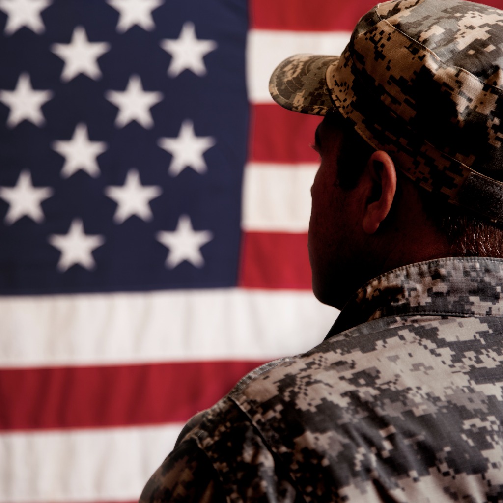 Man in military fatigues standing in front of a U.S. flag suggesting he is one of the celebrities who were in the military.