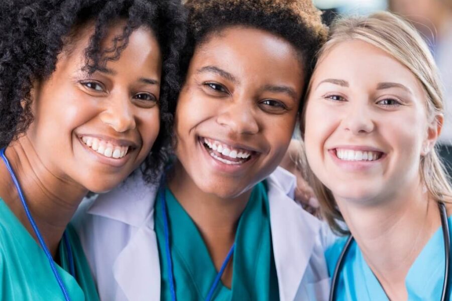 A group of three new nurses wearing their nurse gear in a hospital setting.