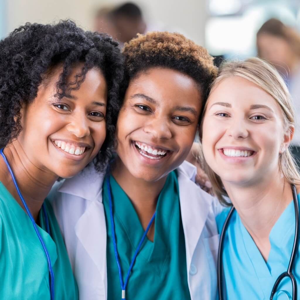 A group of three new nurses wearing their nurse gear in a hospital setting.