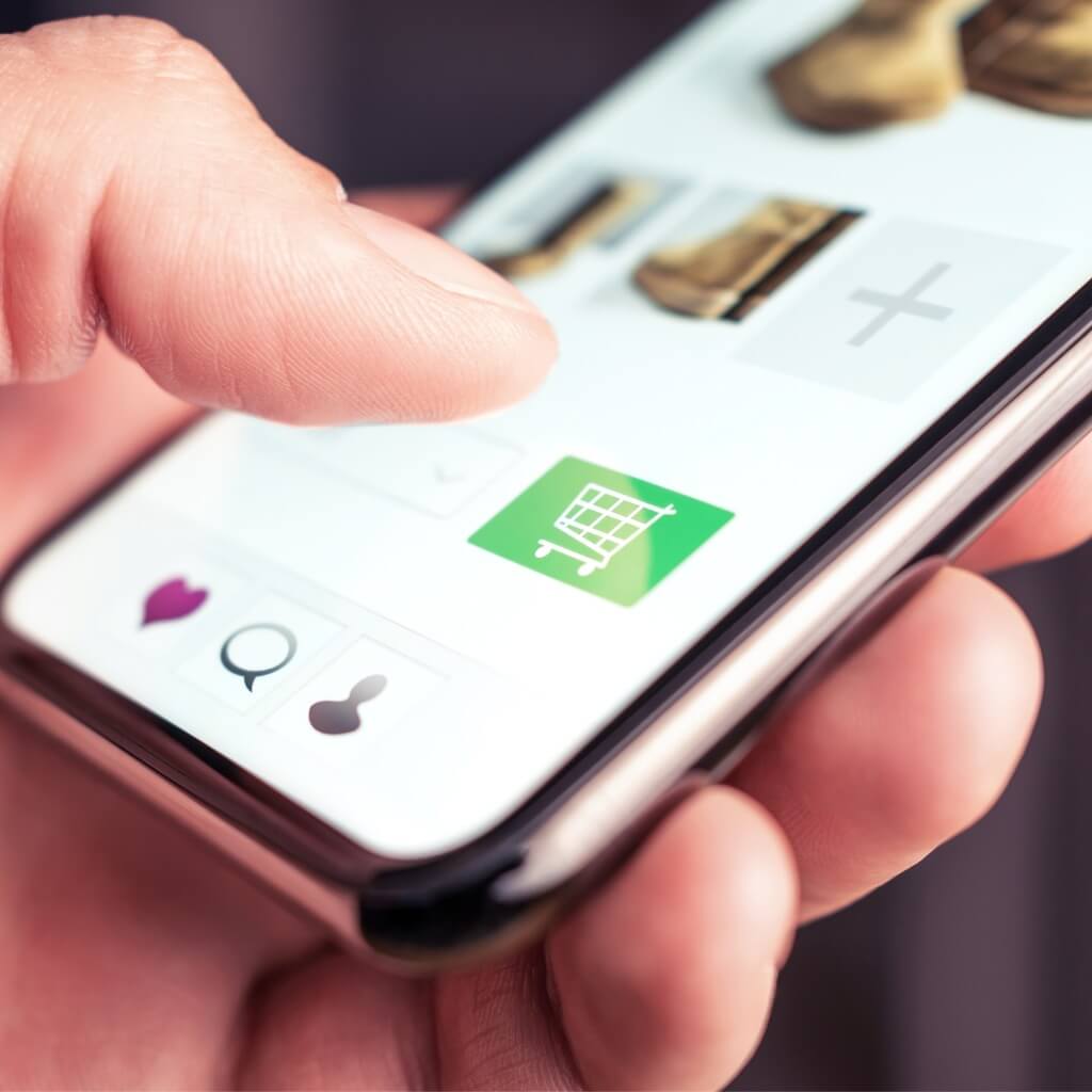 A photo of a person's hand holding a phone with thumb poised over an online store shopping cart.