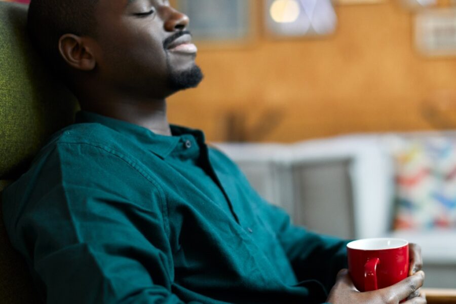 A young Black man in a teal shirt relaxing at home with a cup of tea to beat stress.