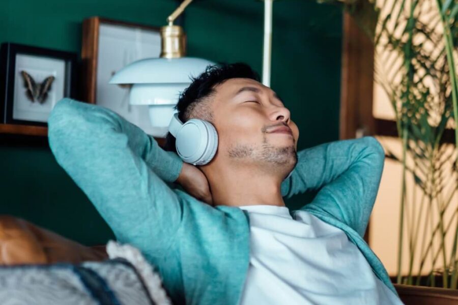 A young Asian man practicing self-care for teachers by listening to music with headphones on.
