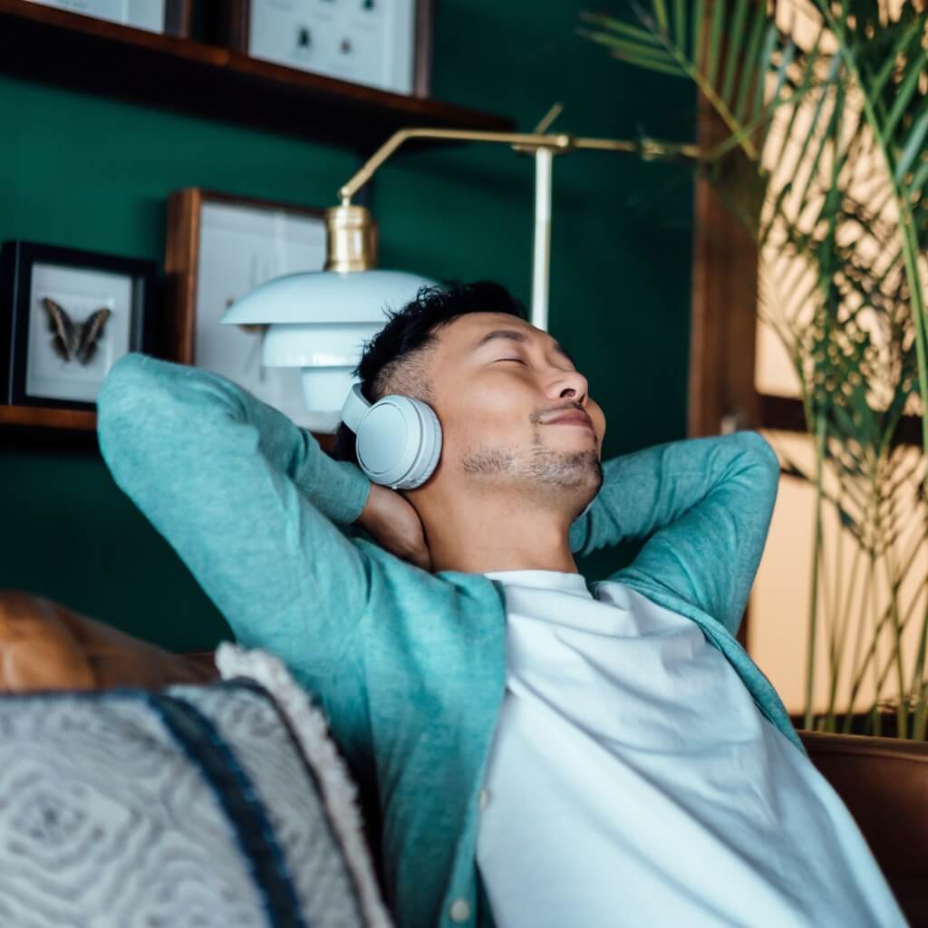 A young Asian man practicing self-care for teachers by listening to music with headphones on.