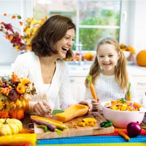 Brunette woman and blonde child cooking food in a fall kitchen with autumn decor.