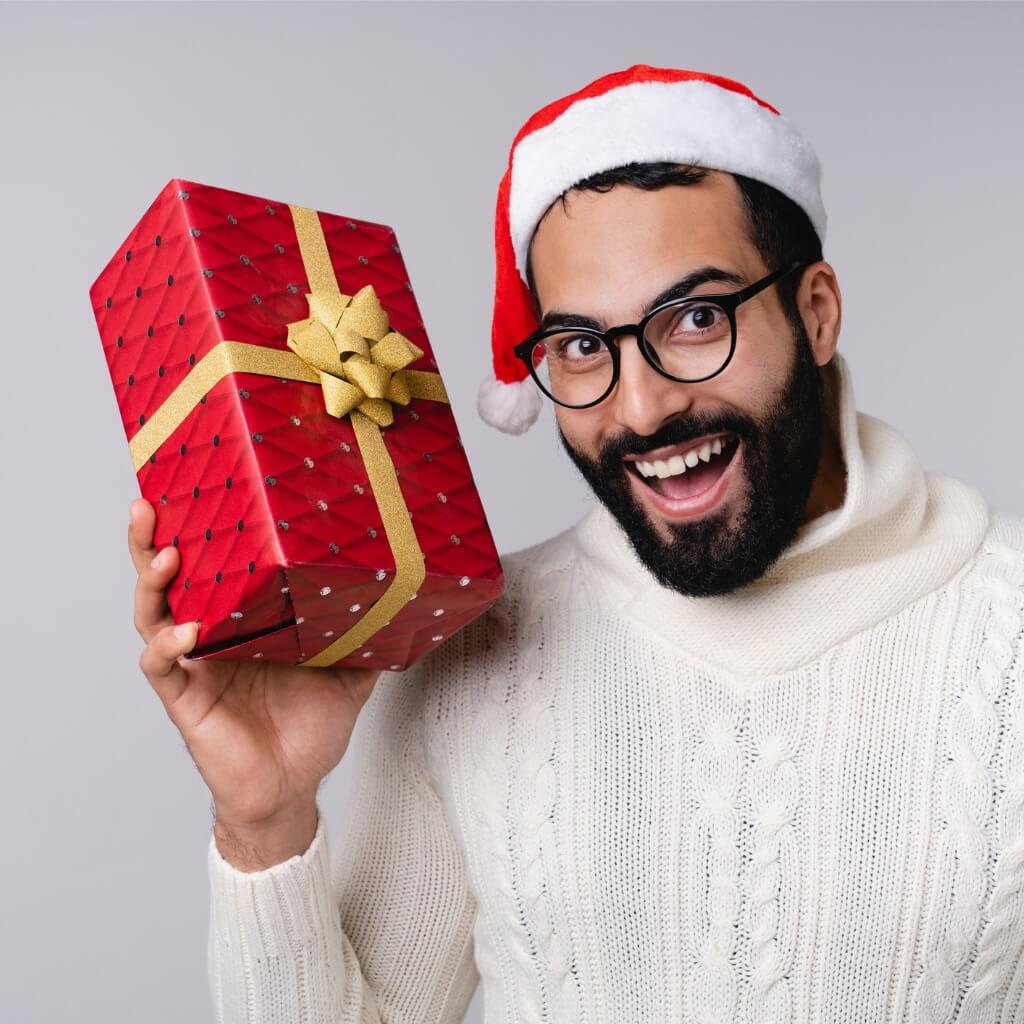 Dark-haired man with a beard holding a wrapped present celebrating first responder holiday discounts.