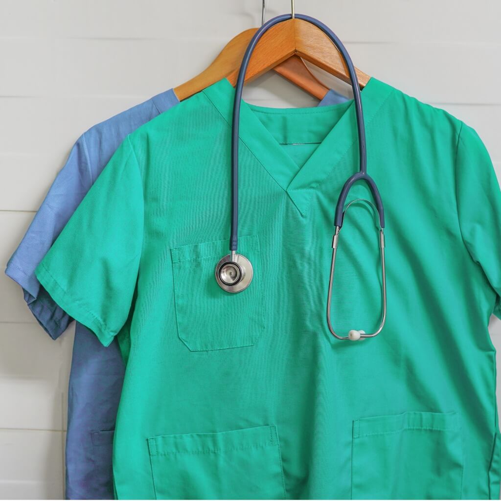 Photo of a clean pair of green scrubs and blue scrubs hanging with a stethoscope.