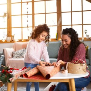 Mother and daughter wrapping gifts in a sunny living room.