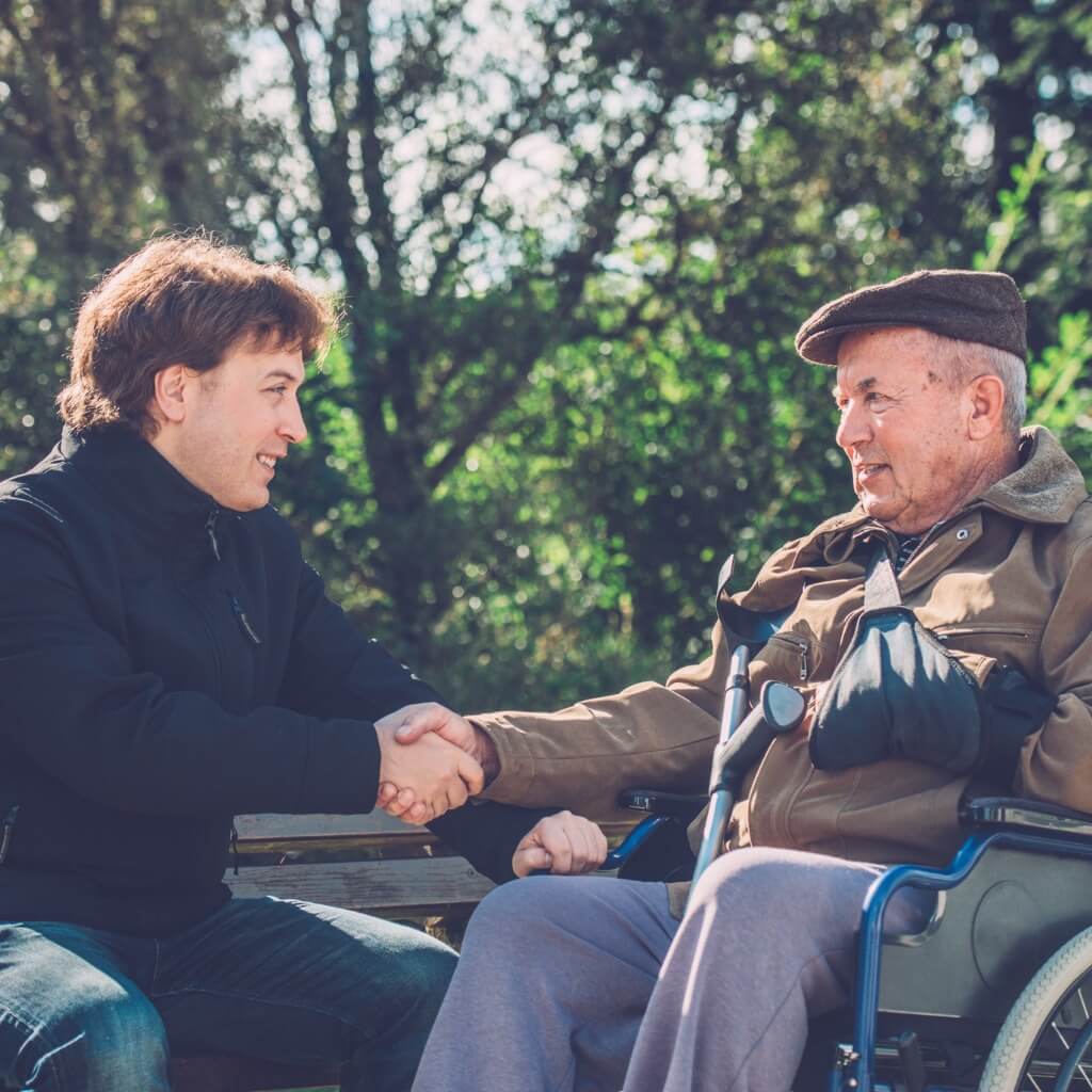 Young man in a park shaking hands with a senior man who is a veteran, thanking him for his service.