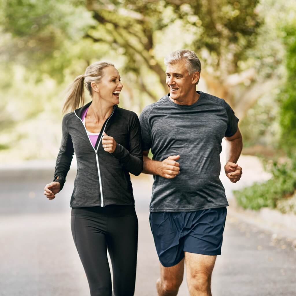 Photo of a middle-aged man and woman in workout clothing jogging along a tree-lined street.